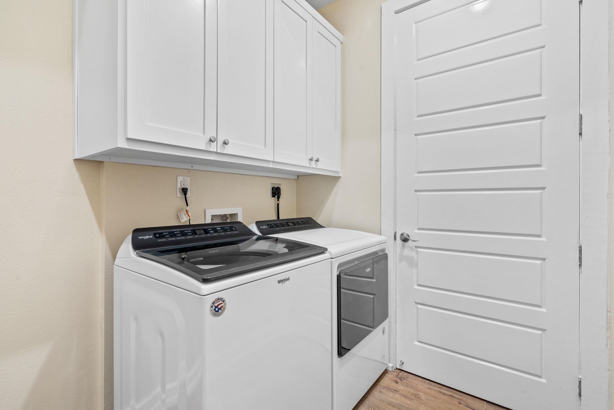 Laundry room with a washer and dryer beneath white cabinets.