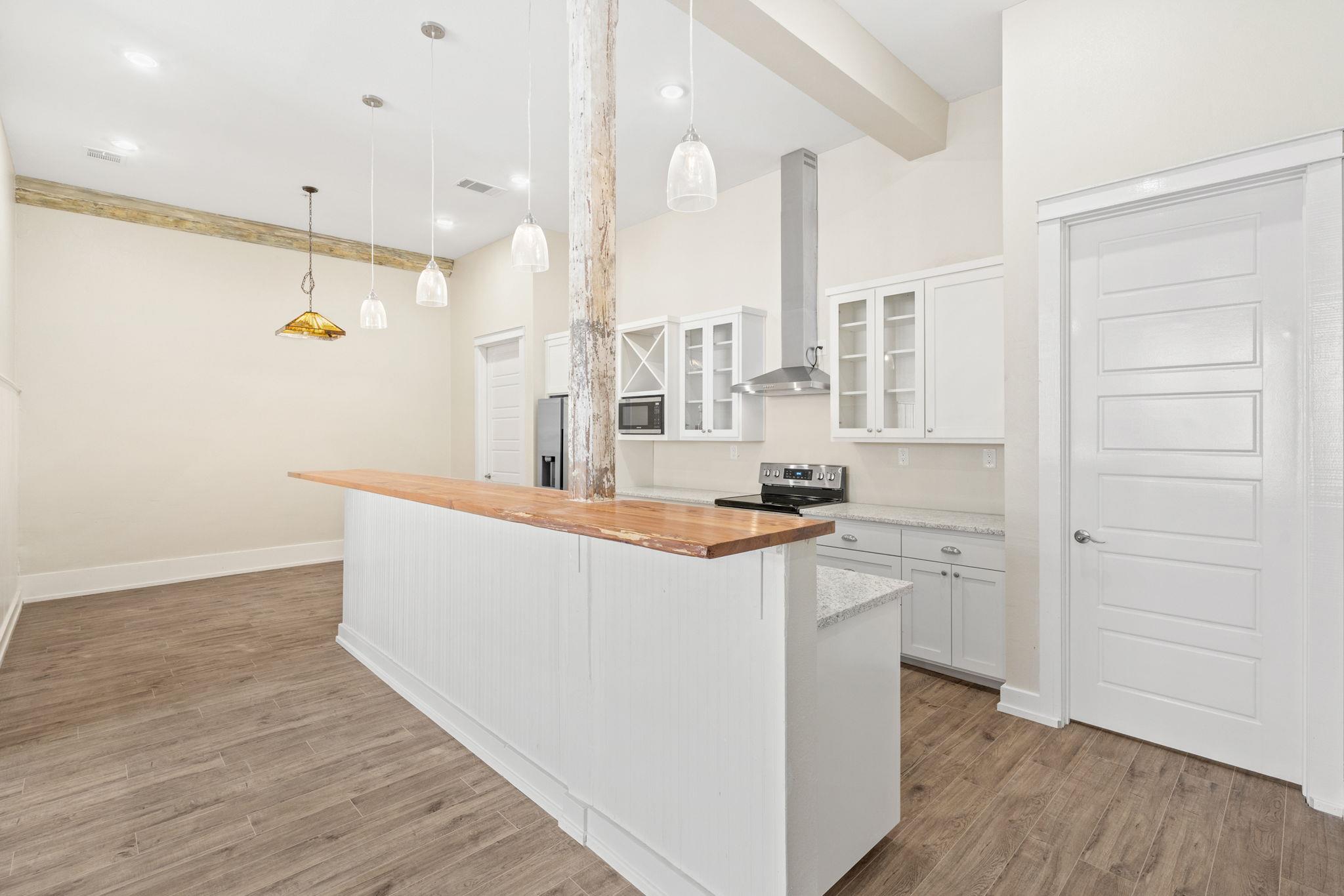Unfurnished kitchen with white cabinets, a butcher-block island, and a distressed wood support post.