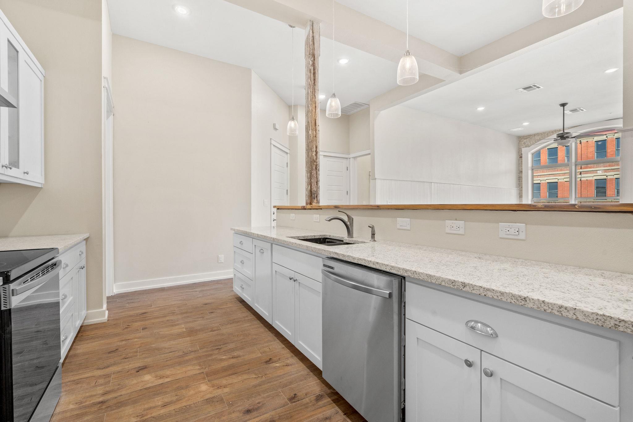 Vacant kitchen with white cabinets, granite counters, stainless dishwasher, and wood-look flooring.