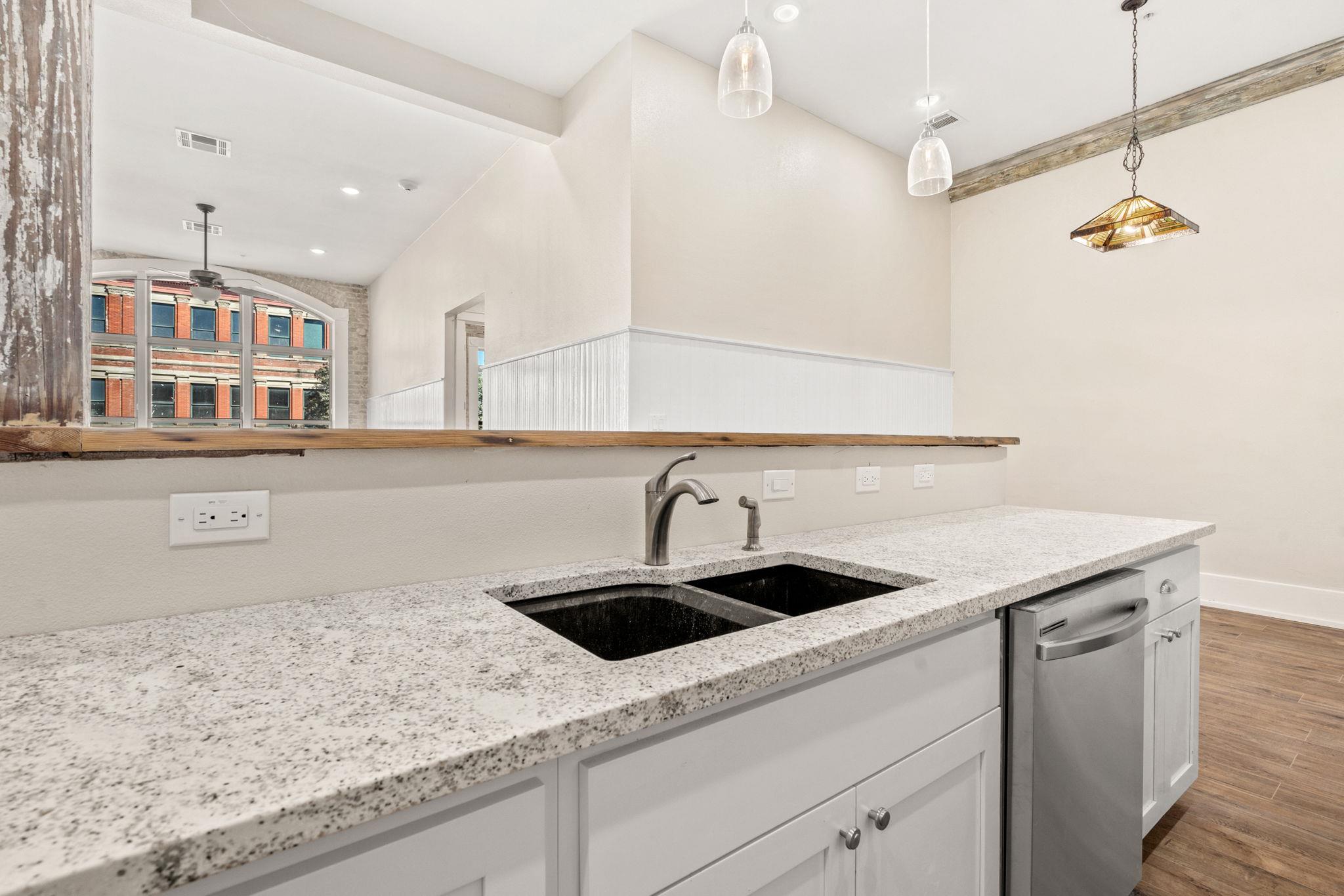 Kitchen with granite counters, a black double sink, stainless dishwasher, and large arched windows.