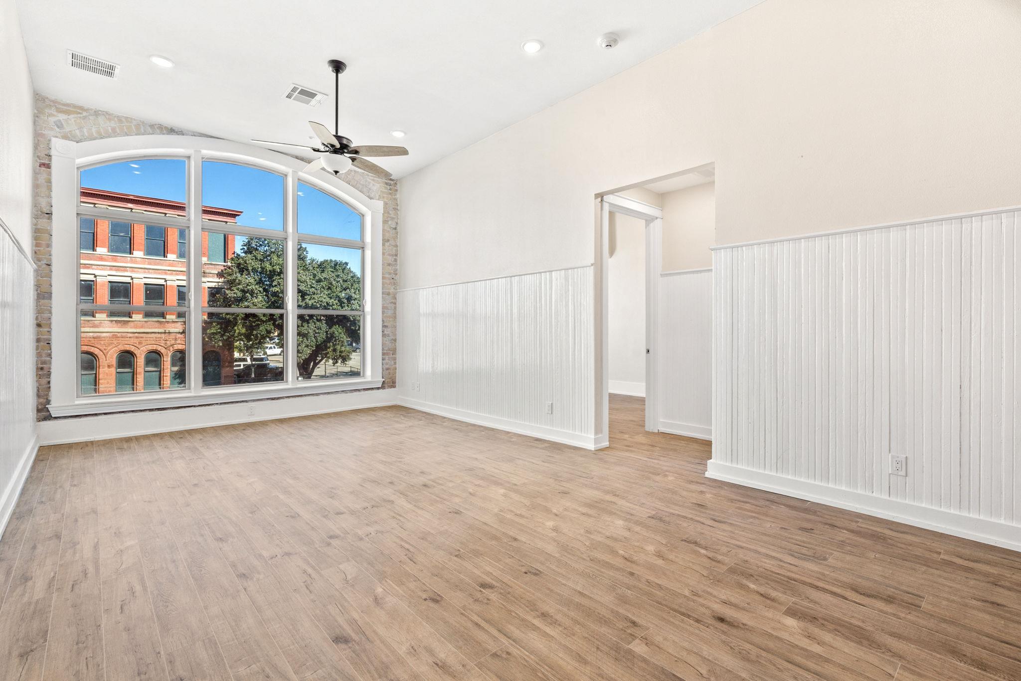 Empty room with wood-look flooring and a large arched window framed by exposed brick.