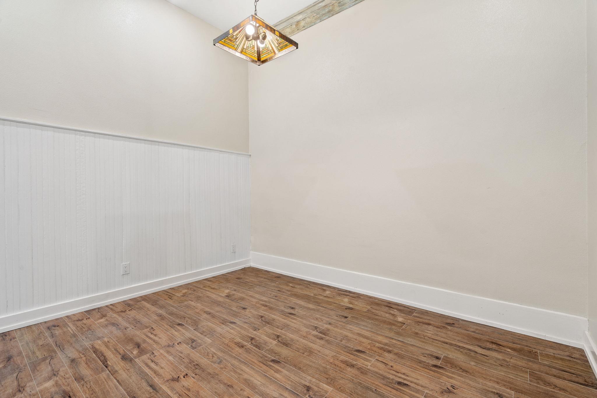 Empty room with wood-look plank floors, white beadboard wainscoting, and a stained-glass-style pendant light.