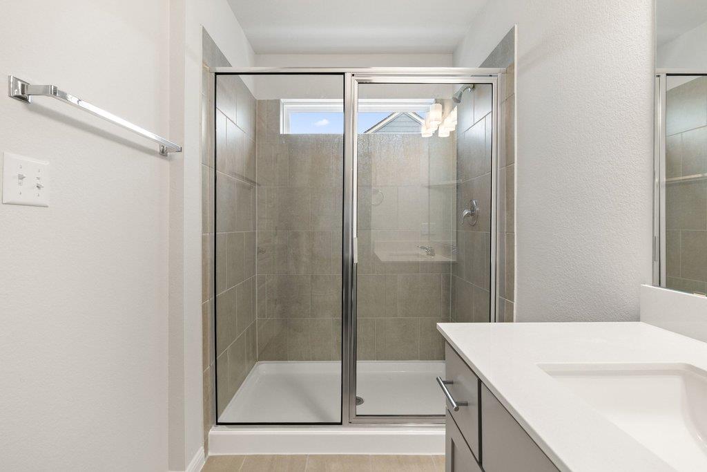 Bathroom with a tiled walk-in shower behind sliding glass doors and a white vanity.