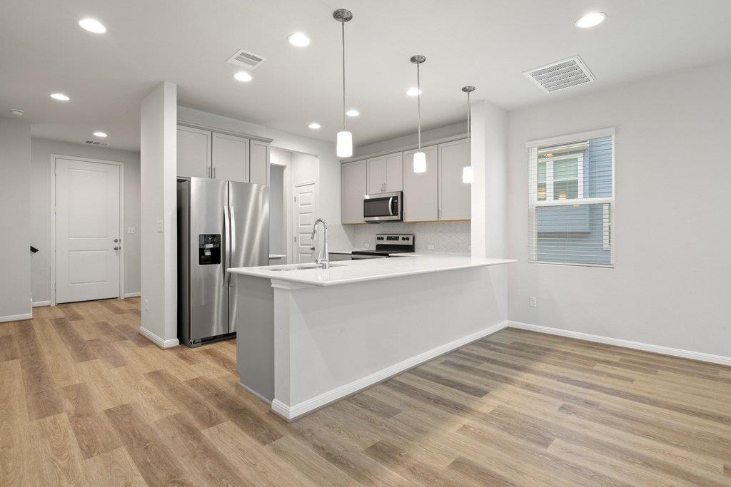 Kitchen with a large white island, stainless steel appliances, and wood-look floors.