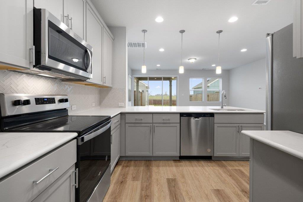 Modern kitchen with gray cabinets, stainless steel appliances, white counters, and sliding glass doors.