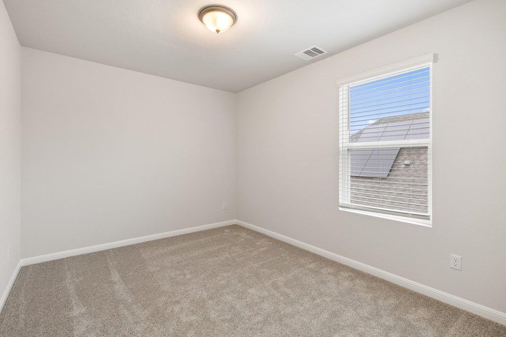 Empty bedroom with beige carpet, white walls, and a window with blinds.