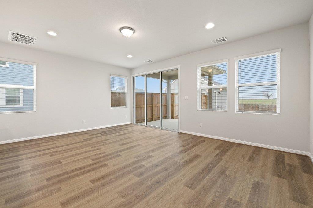 Empty room with wood-look floors, multiple windows, and a sliding glass door to the fenced yard.