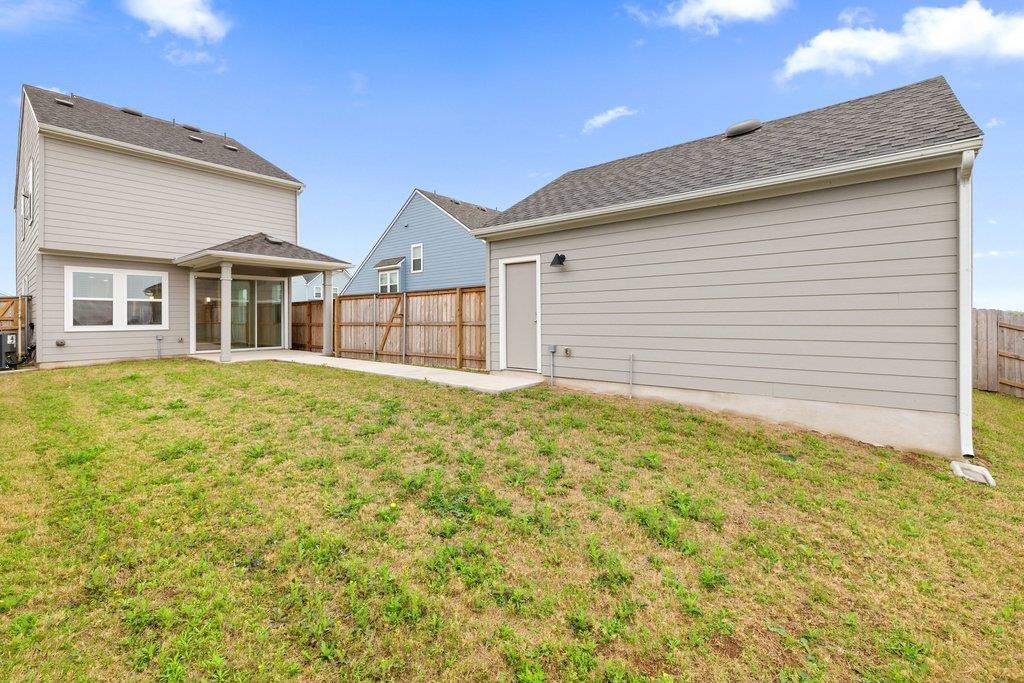 Home’s rear exterior with a fenced lawn, covered patio, and large outbuilding.
