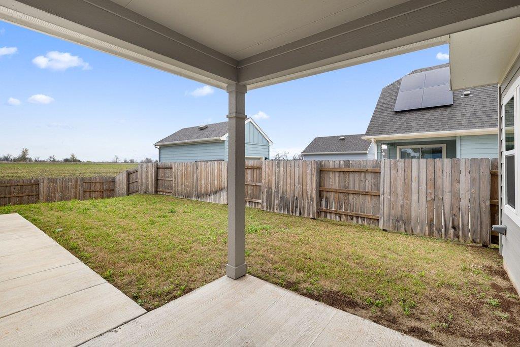 Covered patio overlooking a fenced backyard with patchy grass and neighboring homes.