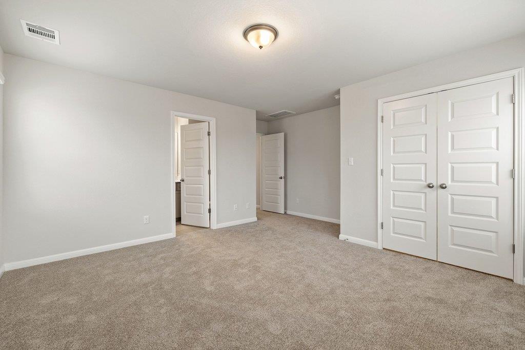 Empty carpeted bedroom with white double closet doors and two doorways along the back wall.