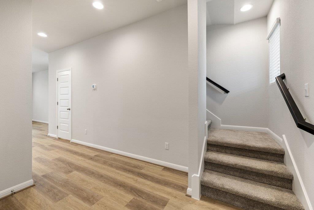 Entry hall with wood-look flooring and carpeted staircase with dark handrails.