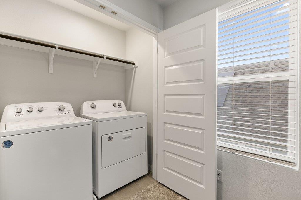 Laundry room with a top-loading washer, front-loading dryer, and large window with blinds.