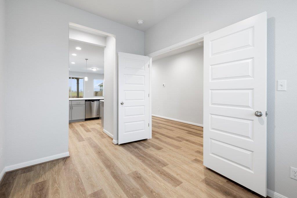 Vacant room with wood-look flooring and open doors, kitchen visible through the doorway.