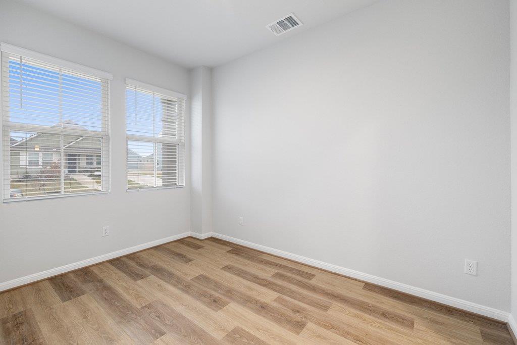 Unfurnished room with wood-look flooring and two windows with blinds.