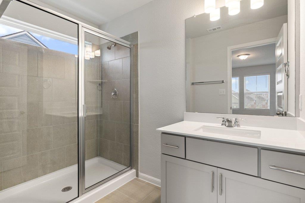 Bathroom with a glass shower and gray tile beside a white vanity and large mirror.