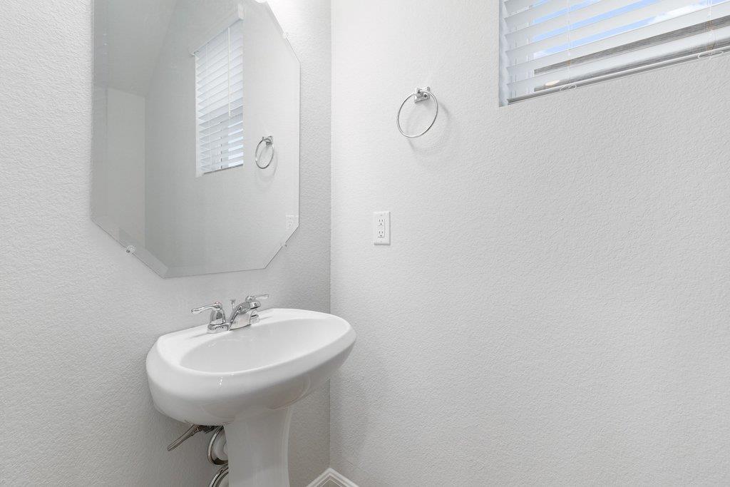 Bathroom pedestal sink with a beveled mirror and a window with white blinds.