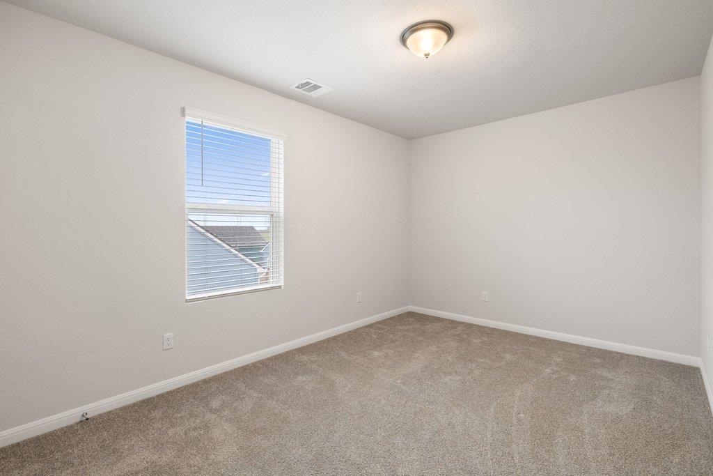 Empty carpeted bedroom with a window fitted with white blinds.