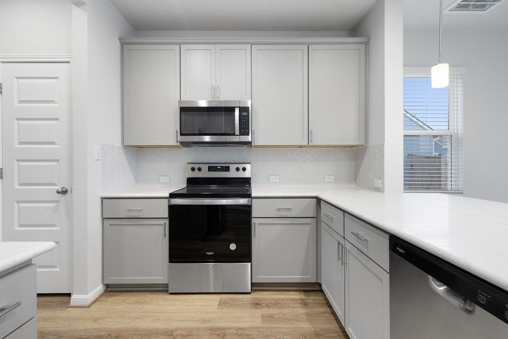 Kitchen with white cabinetry, stainless steel appliances, and a light herringbone backsplash.