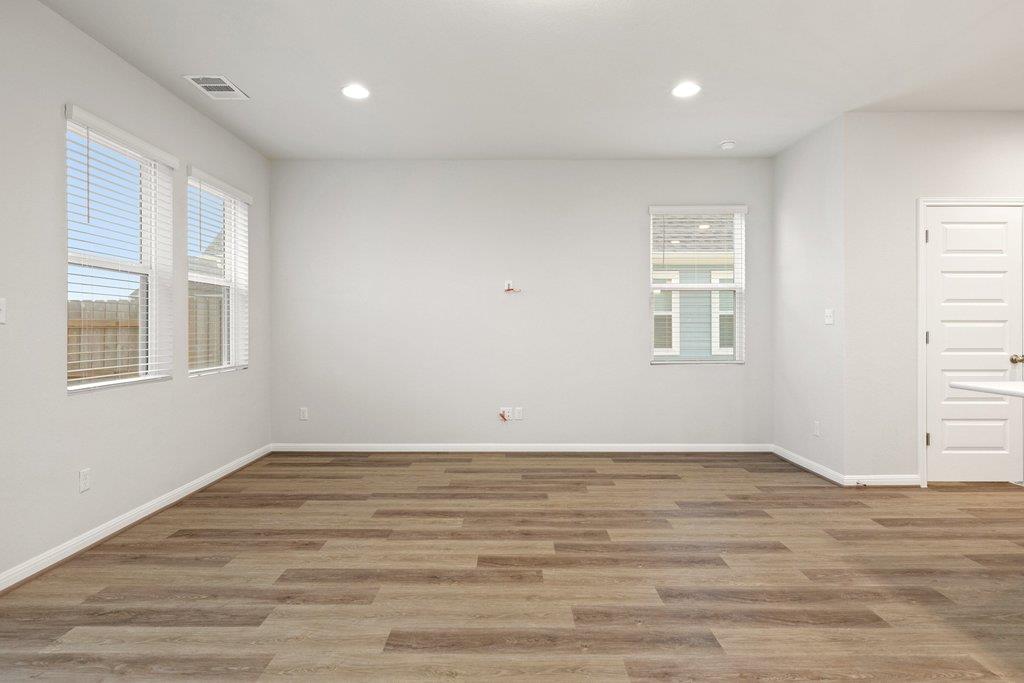 Empty living room with wood-look flooring, several blinded windows, and recessed lights.