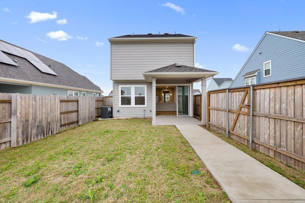 Two-story home's fenced backyard with a covered patio and concrete walkway.
