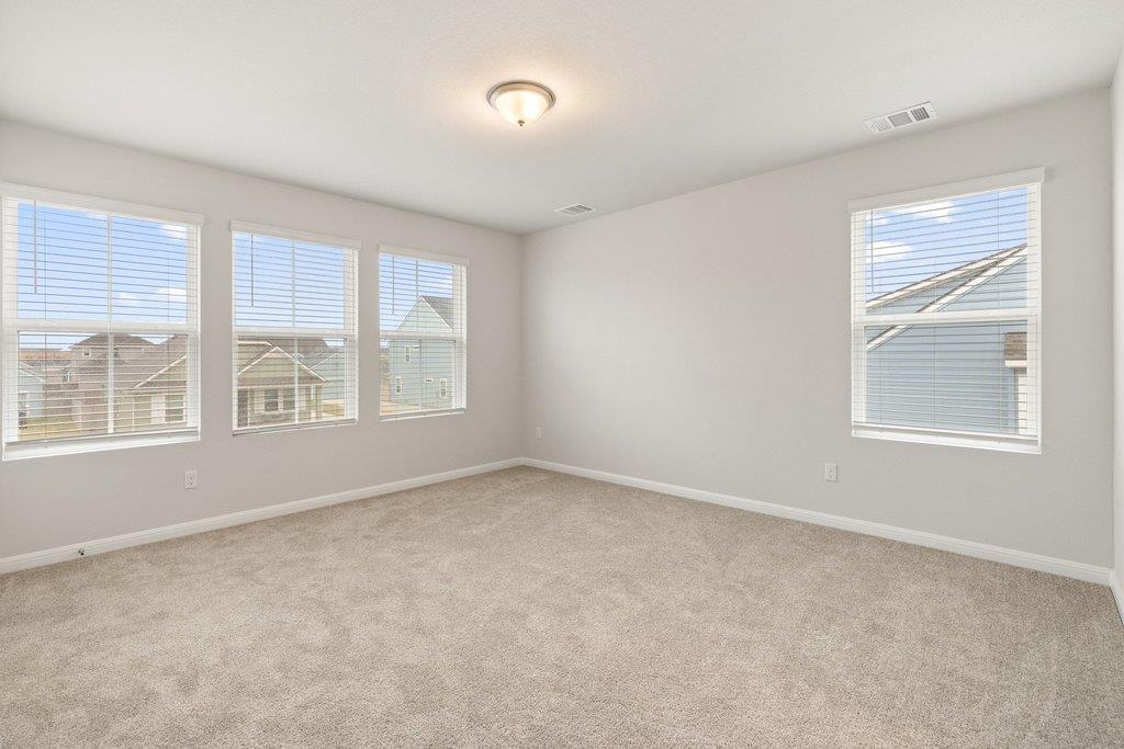Empty carpeted bedroom with four windows and views of neighboring houses.