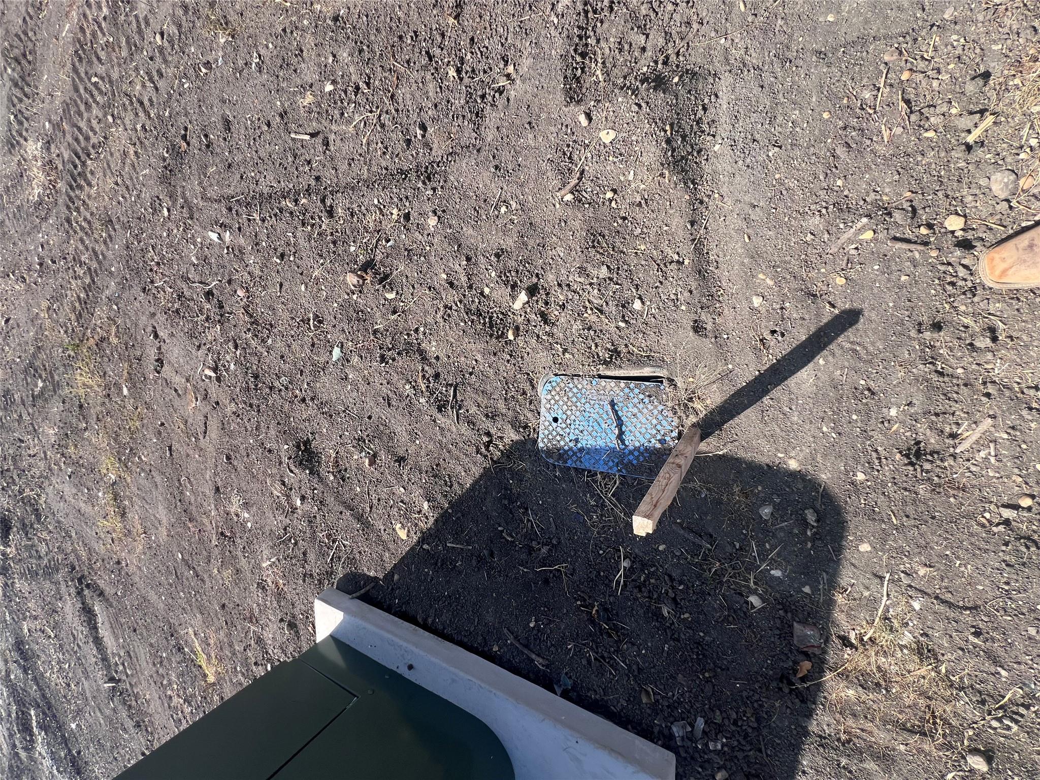 Metal access cover set in bare soil beside a utility box.