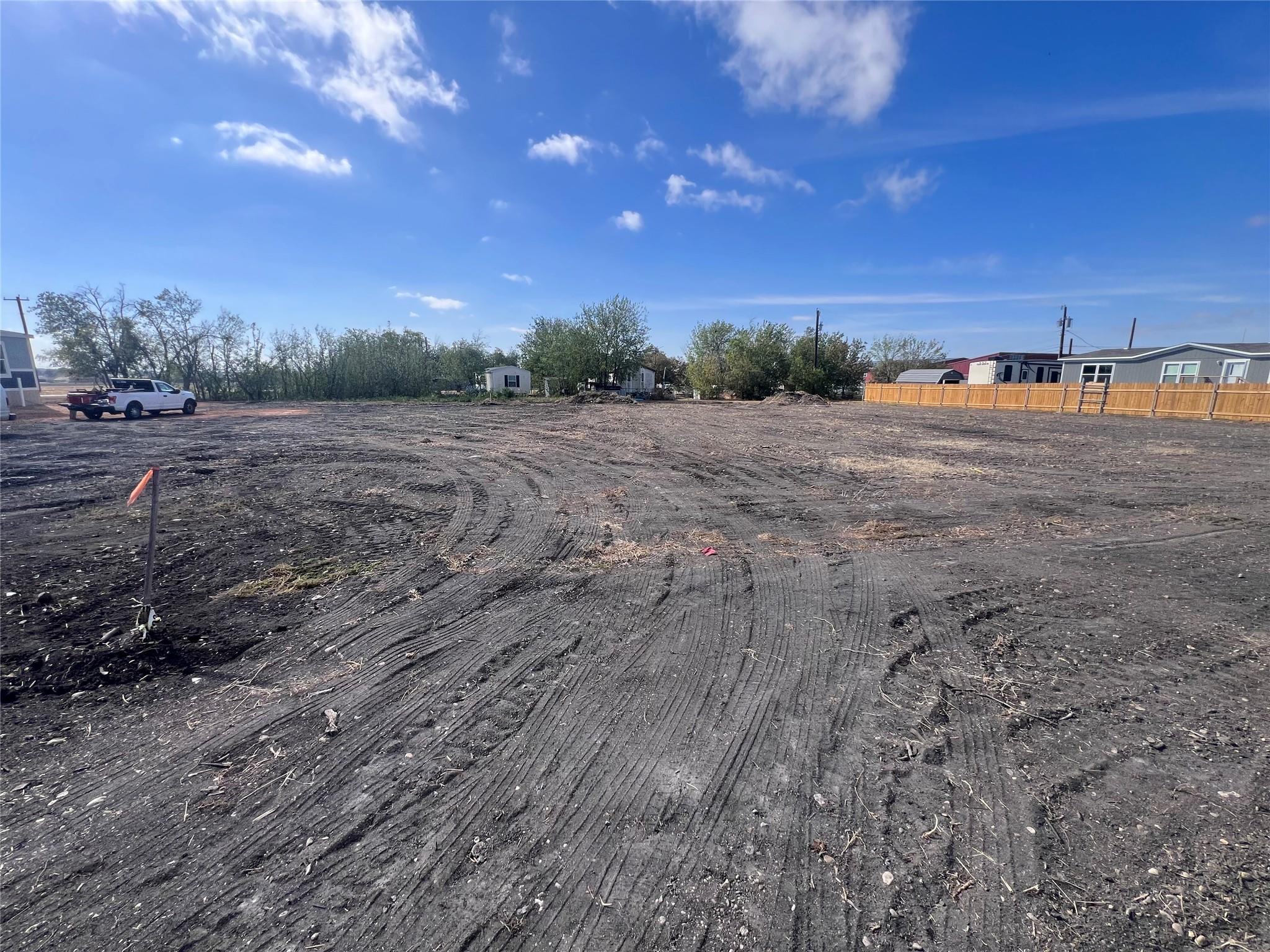 Cleared dirt lot with tire tracks, a survey stake, and neighboring homes along the far edge.