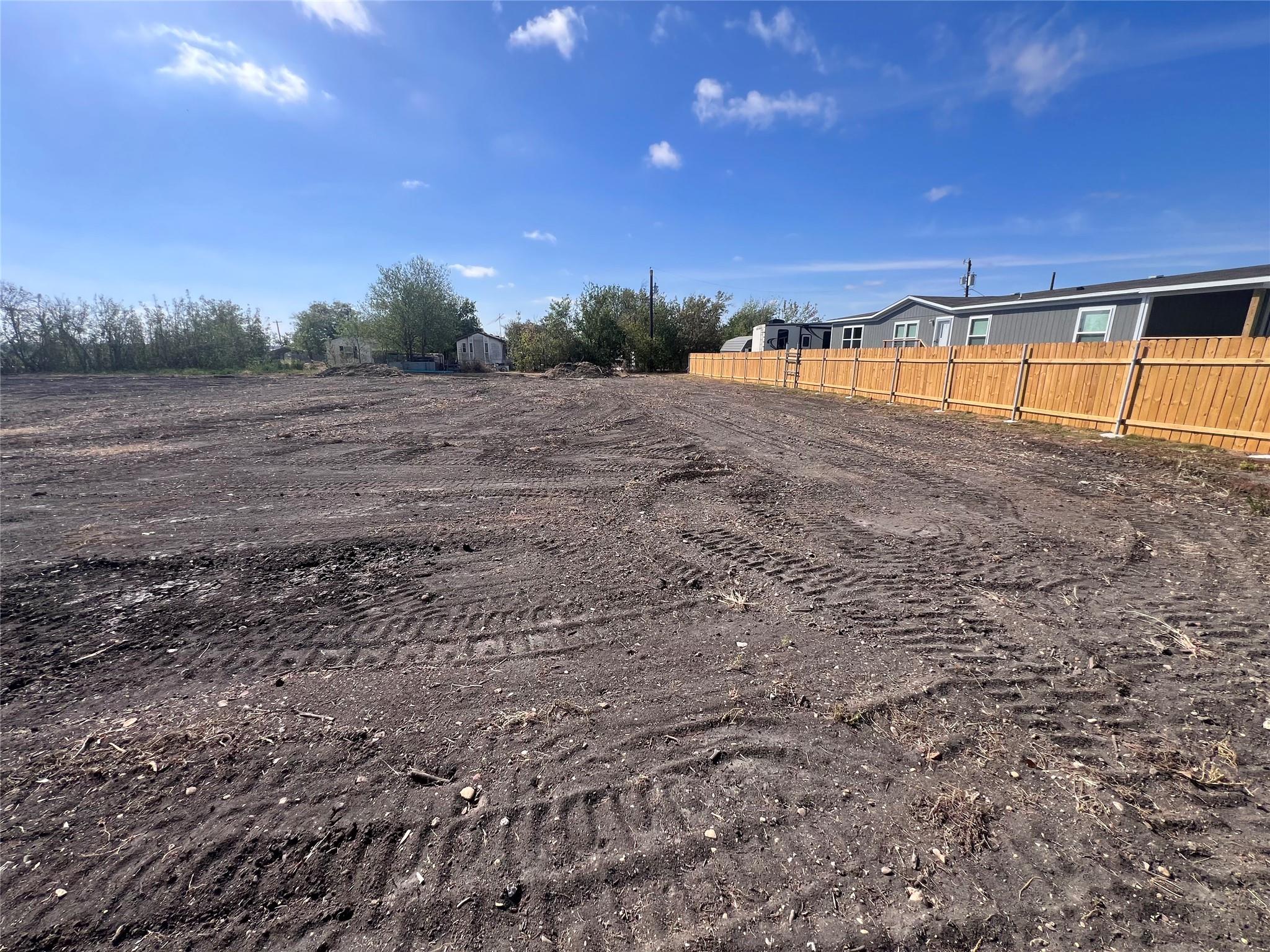 Cleared dirt lot beside a long wooden fence and a manufactured home.