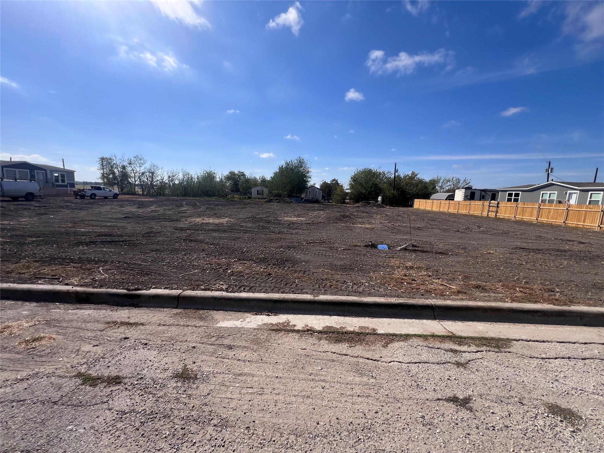 Cleared residential lot with bare soil, neighboring homes, and a wooden fence along the right edge.