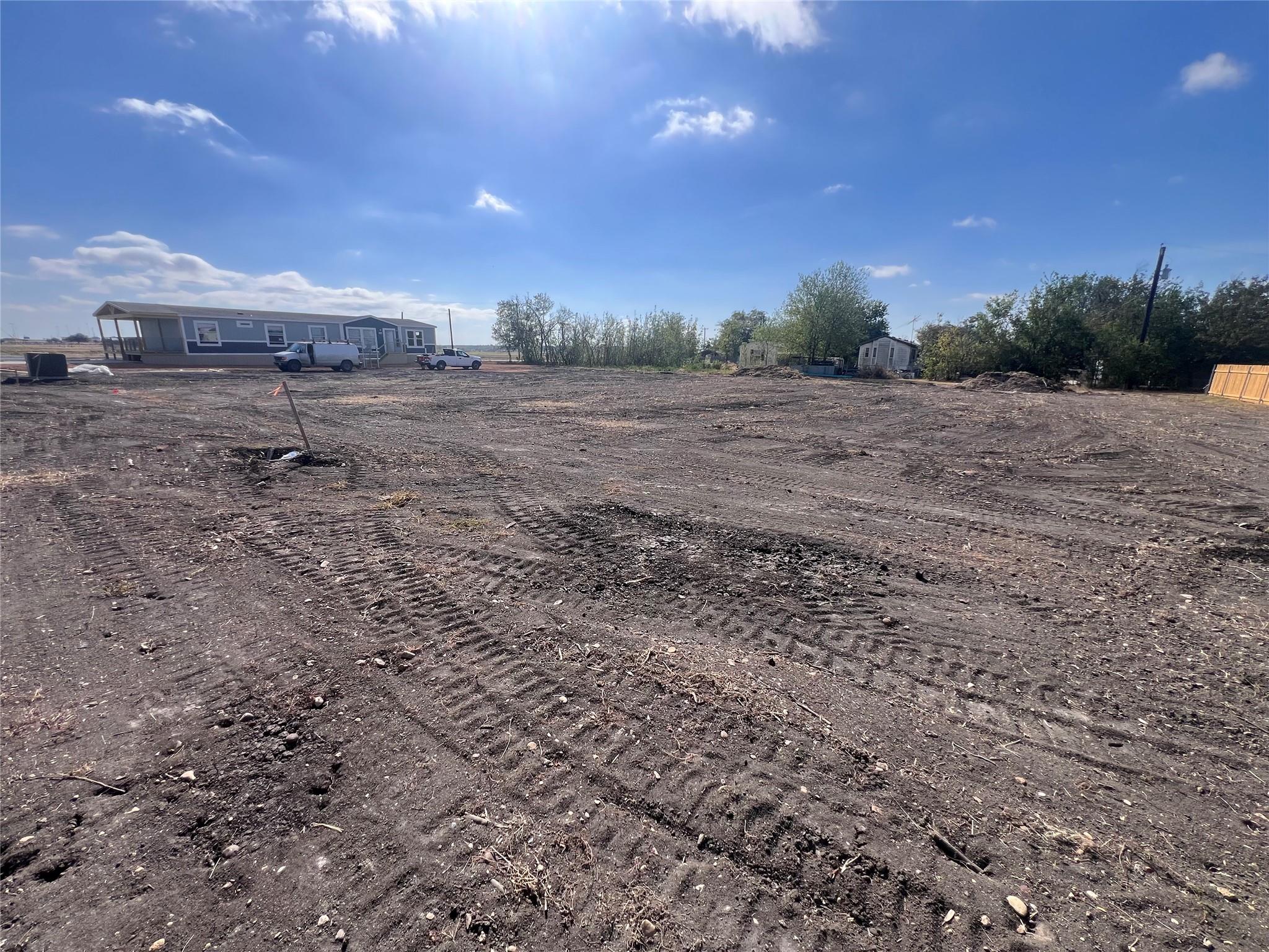 Cleared dirt lot with a manufactured home and vehicles along the far edge.