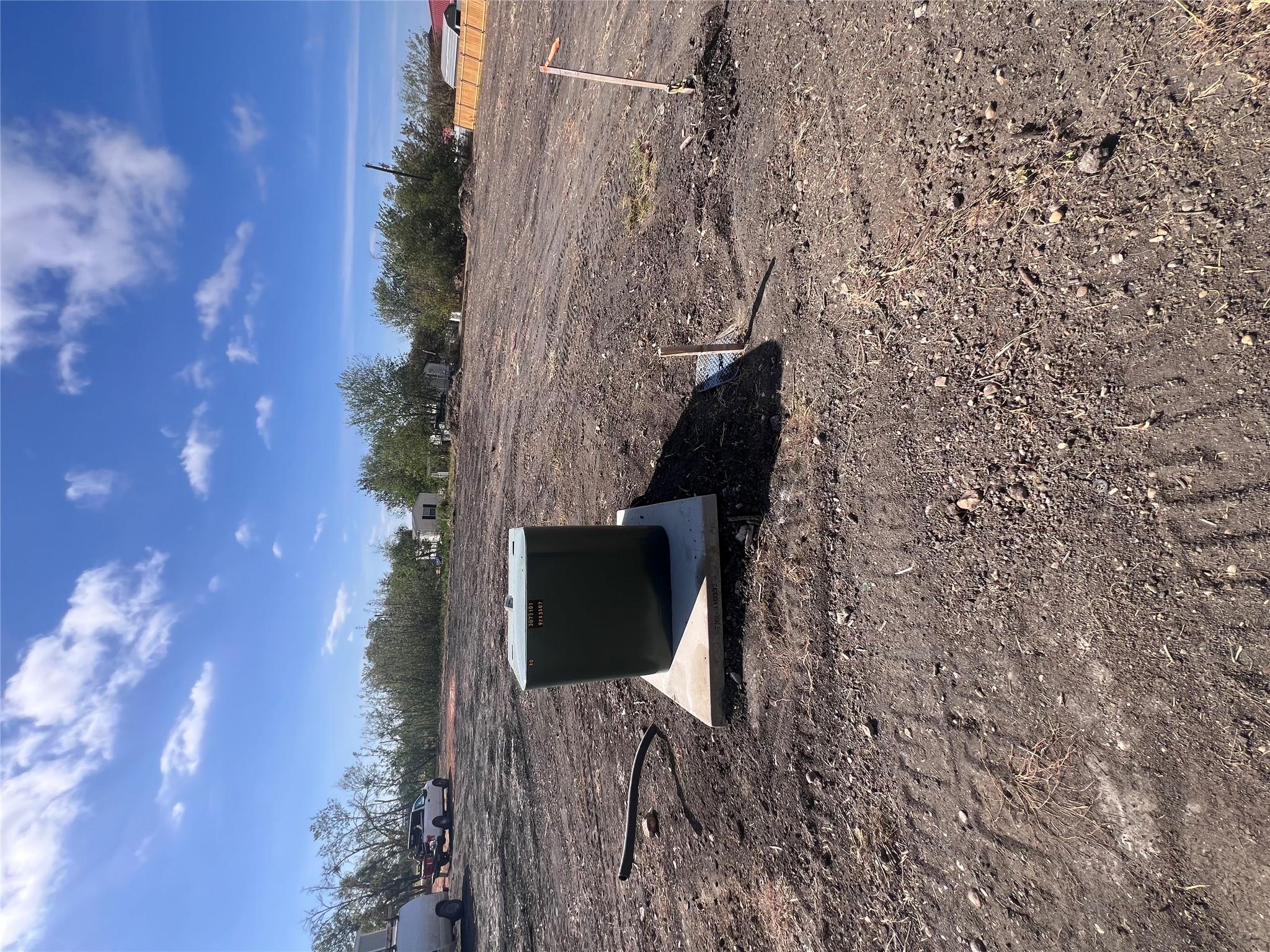 Cleared dirt lot with a utility box on a concrete pad and trees along the far edge.