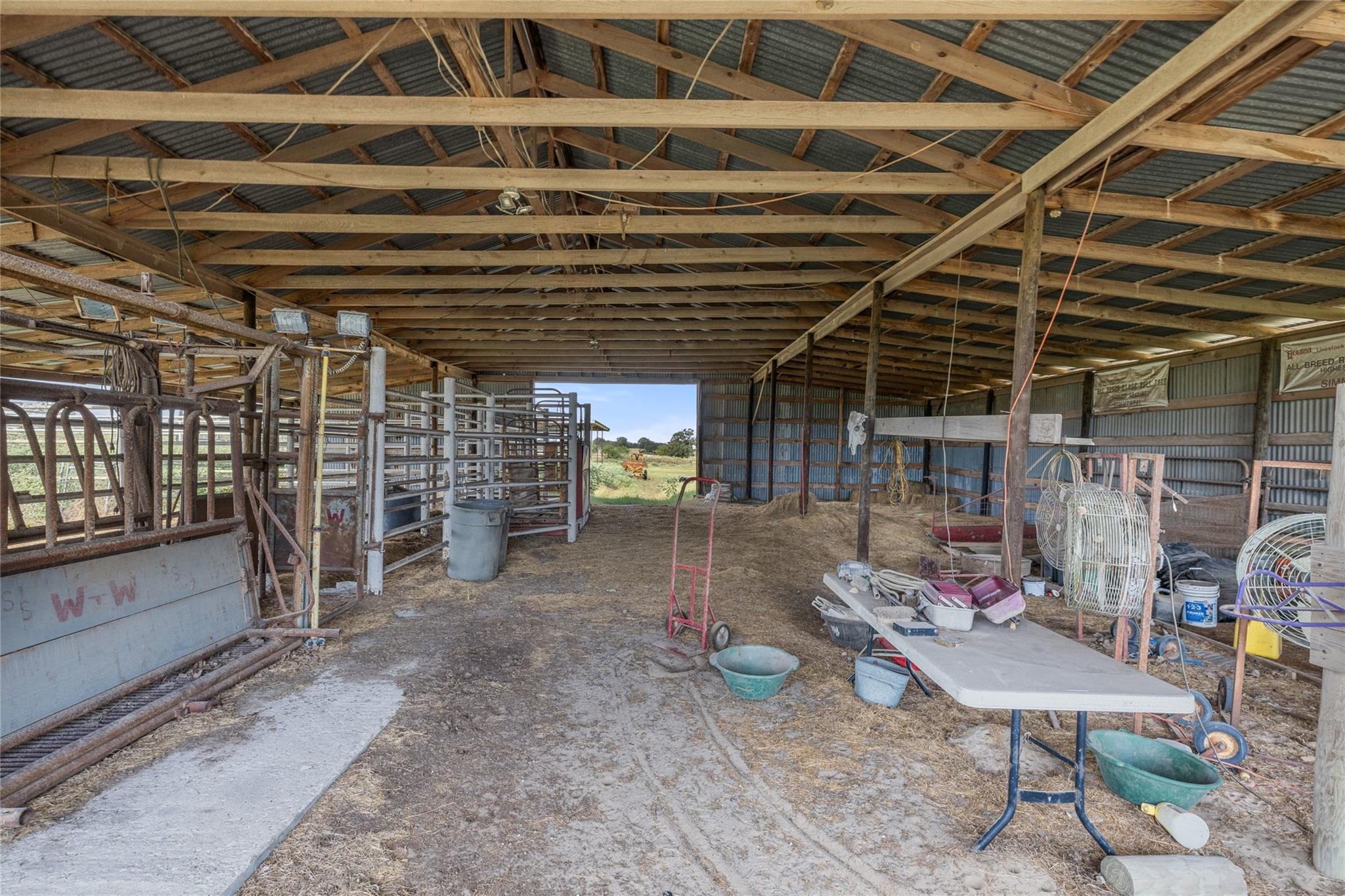 Livestock barn interior with cattle pens, exposed timber trusses, and farm equipment.