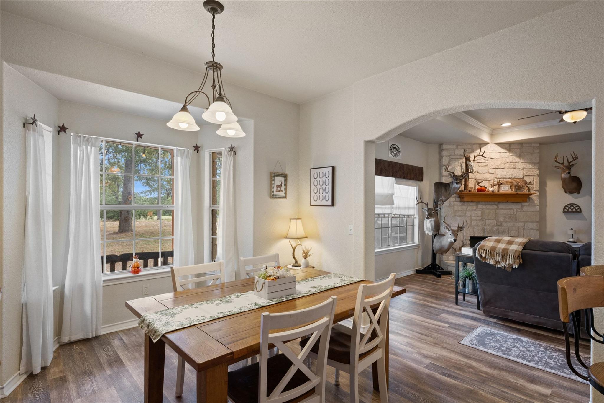 Dining room with a long wooden table and white chairs, opening onto a living room with a stone fireplace.
