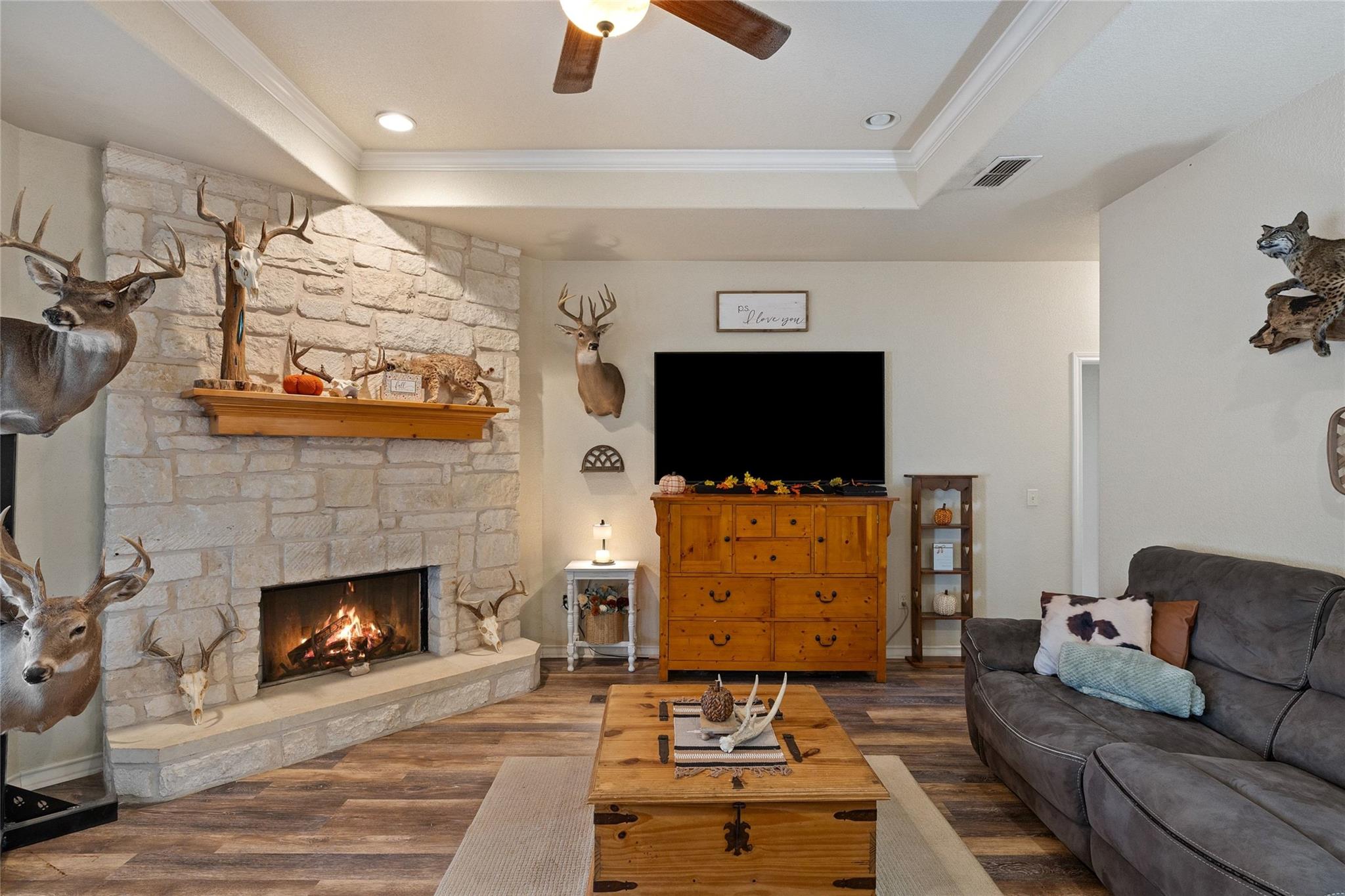 Furnished living room with a stone fireplace, mounted deer, television, and gray sofa.