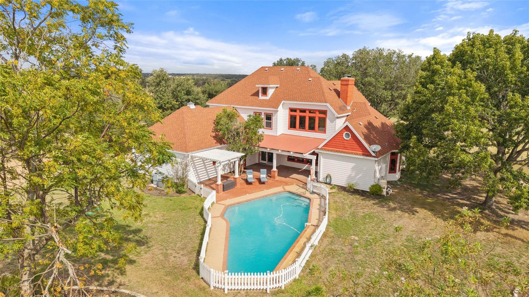 Aerial view of a white house with red trim, a fenced pool, and a covered patio.