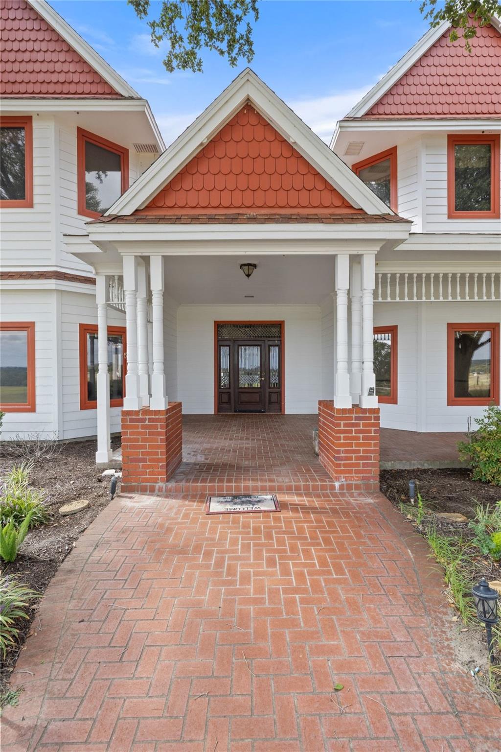 White house with red shingle gables, a columned porch, and a brick walkway.