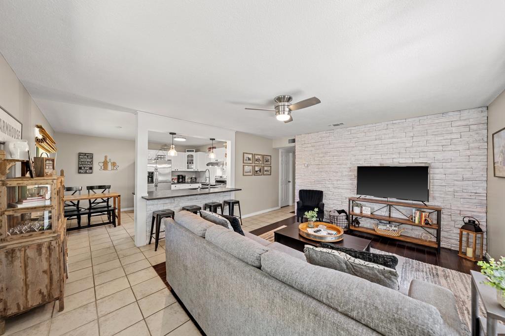 Living room with a white stone accent wall, gray sectional, and open kitchen.