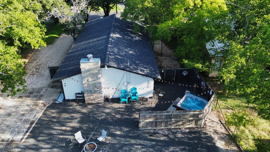 Aerial view of a white house with a fenced hot tub patio beneath mature trees.