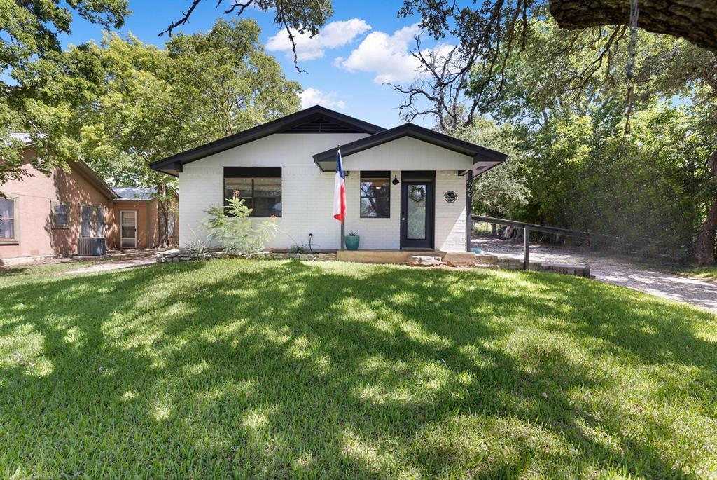White brick house with dark gabled roofs and a Texas flag, set behind a shaded lawn.