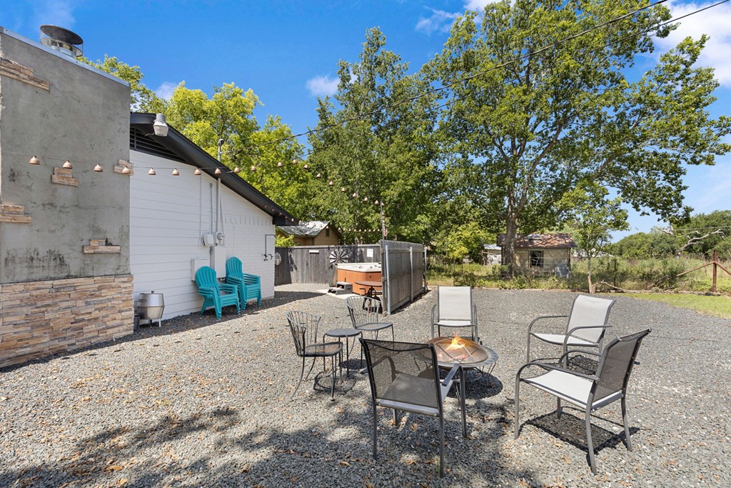 Gravel patio with chairs around a fire pit, string lights, and a hot tub beside the house.
