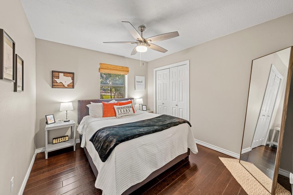Bedroom with a white bed, dark blue throw, wood floors, and a full-length mirror.