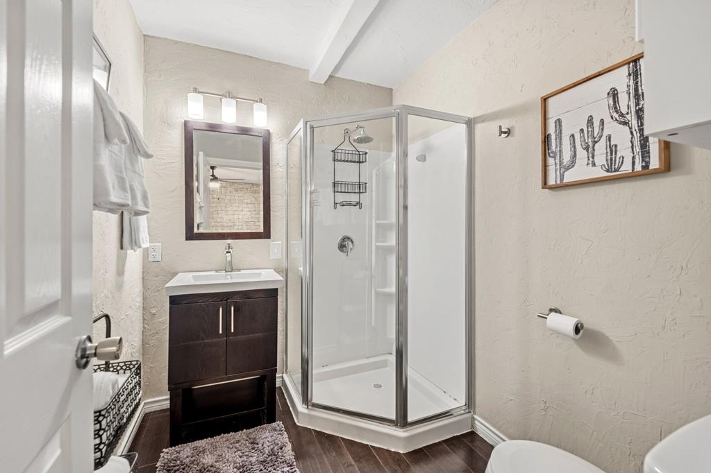 Bathroom with glass corner shower, dark wood vanity, and framed cactus artwork.