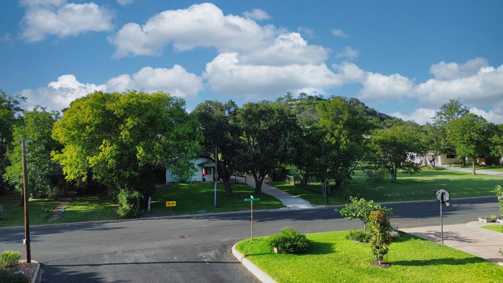 Tree-shaded house partly hidden by mature trees, with a wooded hill behind it.