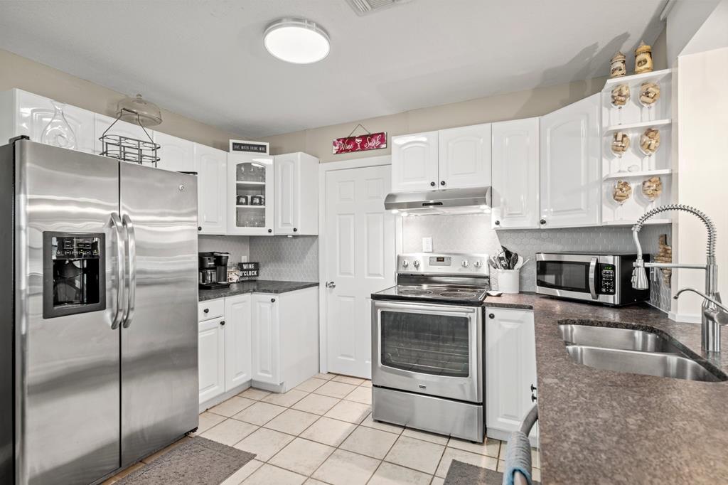 White kitchen with stainless appliances, dark countertops, and a double-basin sink.