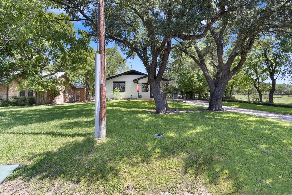 Single-story home behind a shaded lawn, framed by large oak trees.