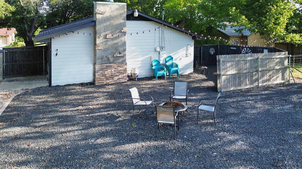 Gravel patio with outdoor chairs beside a white house and stone chimney.