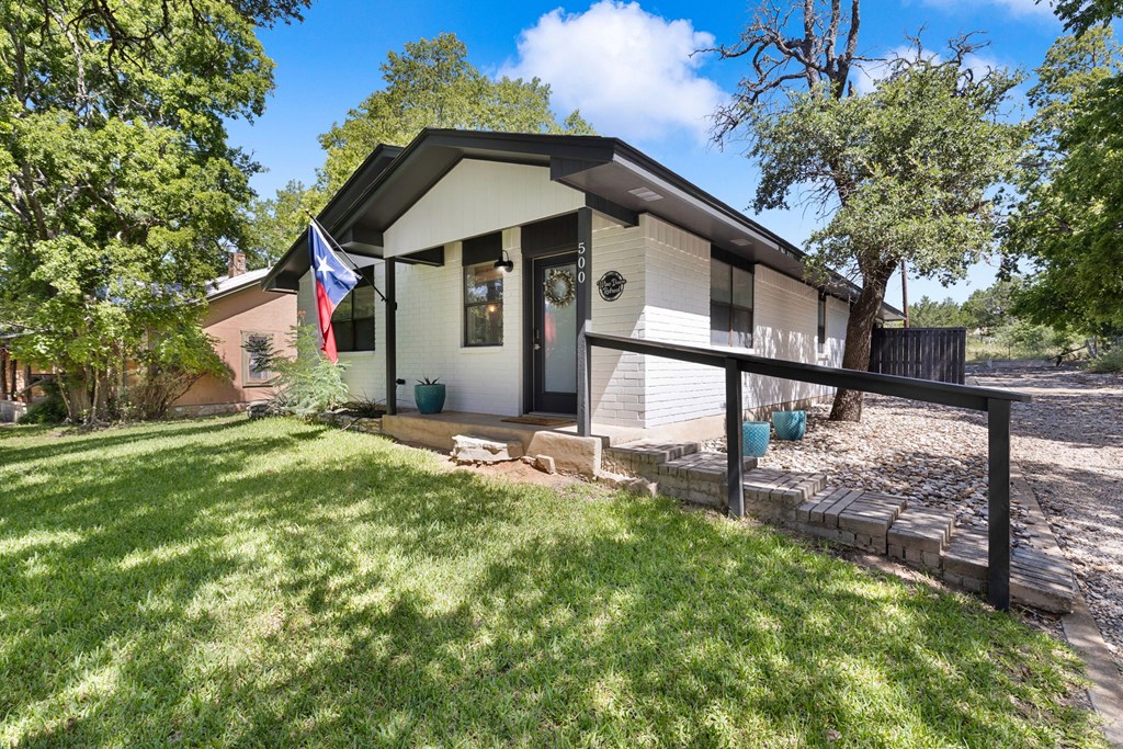 White home with dark trim, Texas flag, and accessibility ramp beneath mature trees.