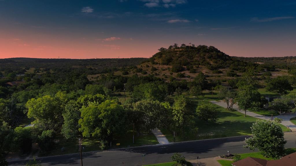 Aerial view of a wooded neighborhood and rocky hill beneath a pink dusk sky.