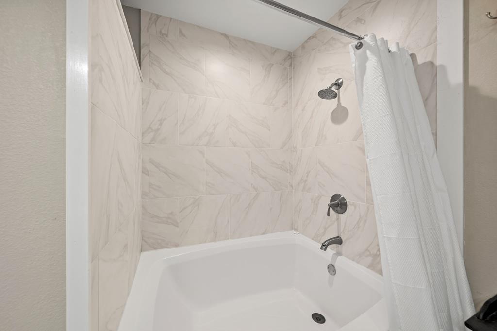 Bathroom tub and shower with marble-pattern tile and chrome fixtures.