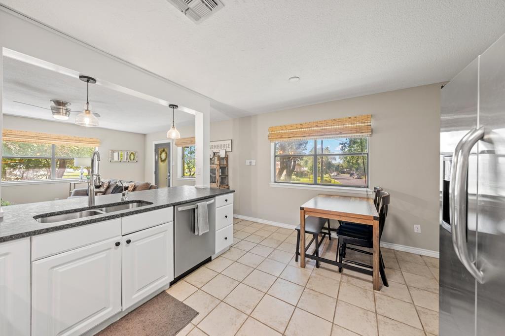 Kitchen with white cabinets and stone counters, opening to a dining nook beside a large window.